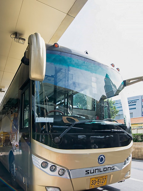 Tour bus parked at a station in Bangkok, Thailand, with passengers boarding.