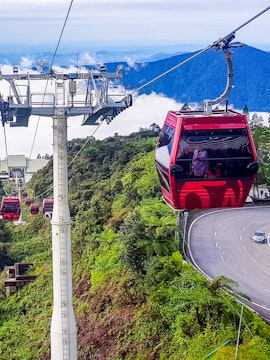 Genting Awana Cable Car ascending over lush green hills with a winding road below.