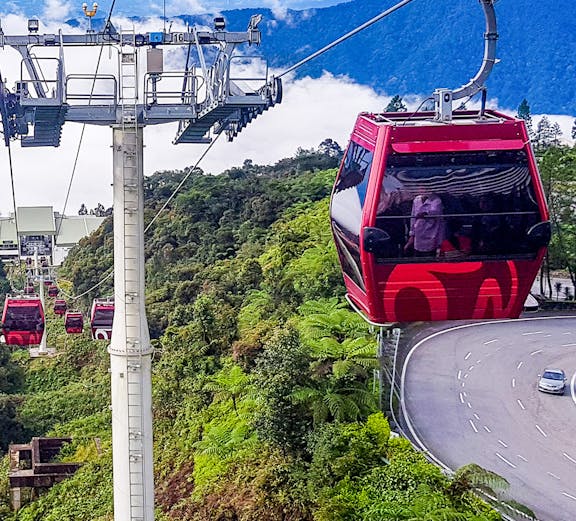 Genting Awana Cable Car ascending over lush green hills with a winding road below.