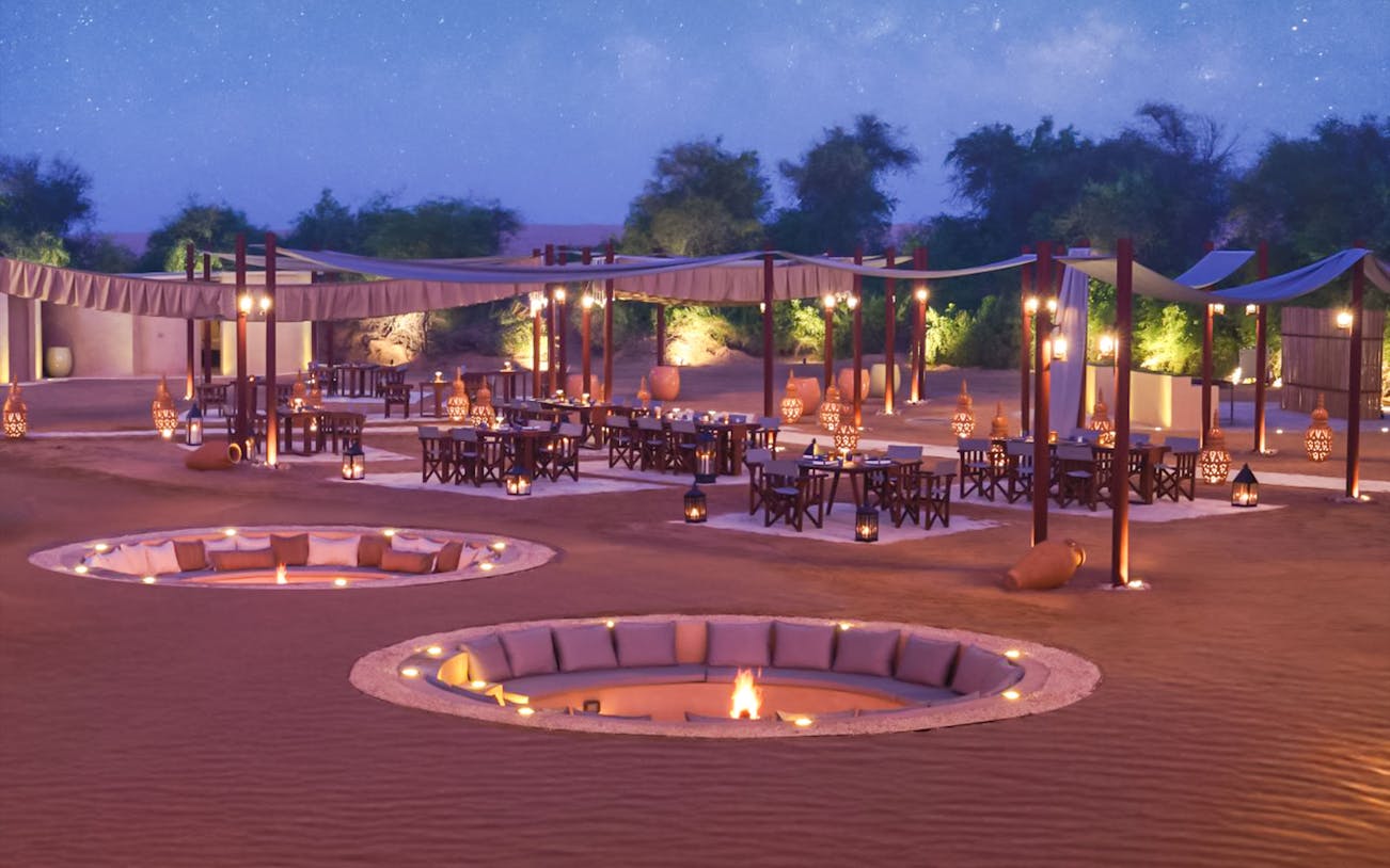 Desert dining setup with fire pits and lanterns at The Nomad Garden.