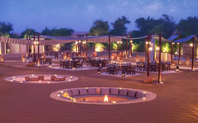 Desert dining setup with fire pits and lanterns at The Nomad Garden.