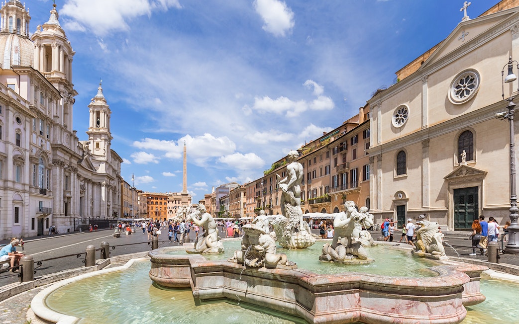 Tourists walking by the Fountain of Neptune in Piazza Navona, Rome.