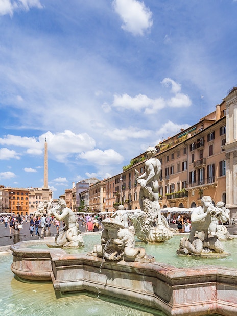 Tourists walking by the Fountain of Neptune in Piazza Navona, Rome.