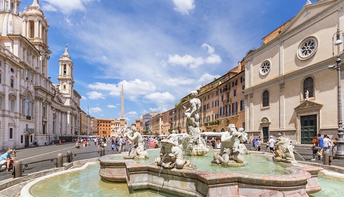 Tourists walking by the Fountain of the Four Rivers in Piazza Navona, Rome.