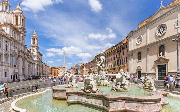 Tourists walking by the Fountain of Neptune in Piazza Navona, Rome.