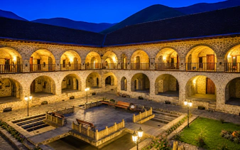 Courtyard of historic Sheki Caravanserai lit at night, featuring stone arches and benches, Sheki, Azerbaijan.