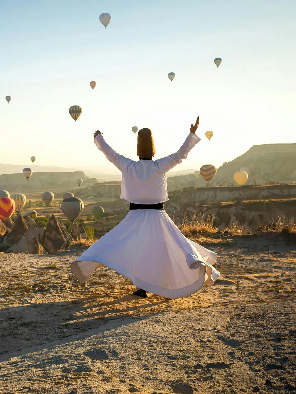 Whirling dervish performing in Cappadocia with hot air balloons in the background.