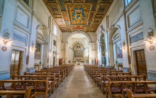 Interior of Basilica of San Sebastiano in Rome with ornate ceiling and wooden pews.