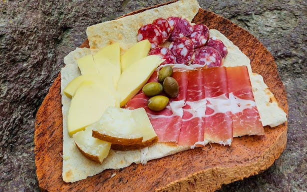 Charcuterie board with cured meats, cheeses, olives, and flatbread on a wooden platter.