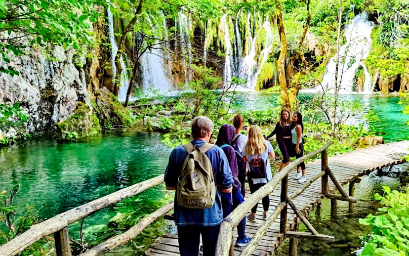 Visitors walking on a wooden path by waterfalls in Plitvice Lakes National Park.