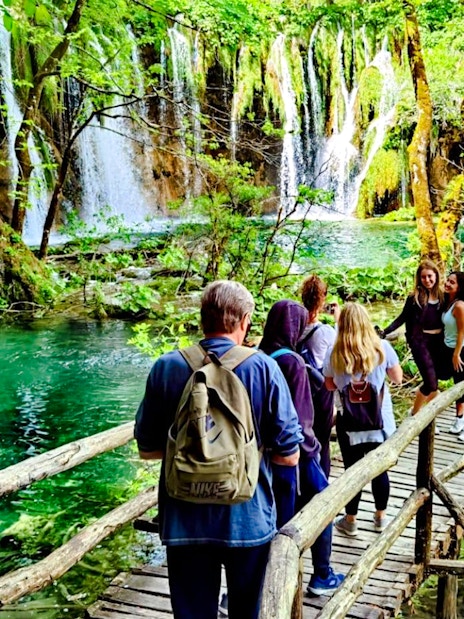 Visitors walking on a wooden path by waterfalls in Plitvice Lakes National Park.