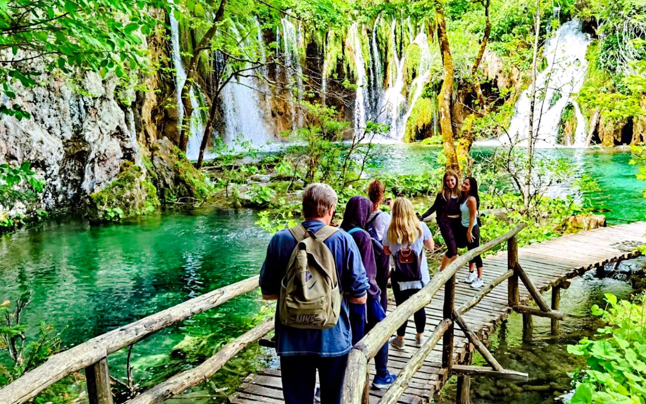 Visitors walking on a wooden path by waterfalls in Plitvice Lakes National Park.