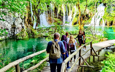 Visitors walking on a wooden path by waterfalls in Plitvice Lakes National Park.