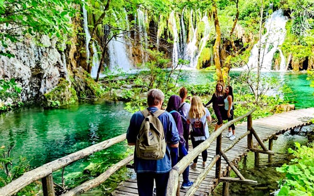 Visitors walking on a wooden path by waterfalls in Plitvice Lakes National Park.