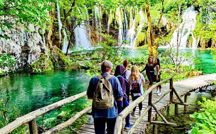 Visitors walking on a wooden path by waterfalls in Plitvice Lakes National Park.