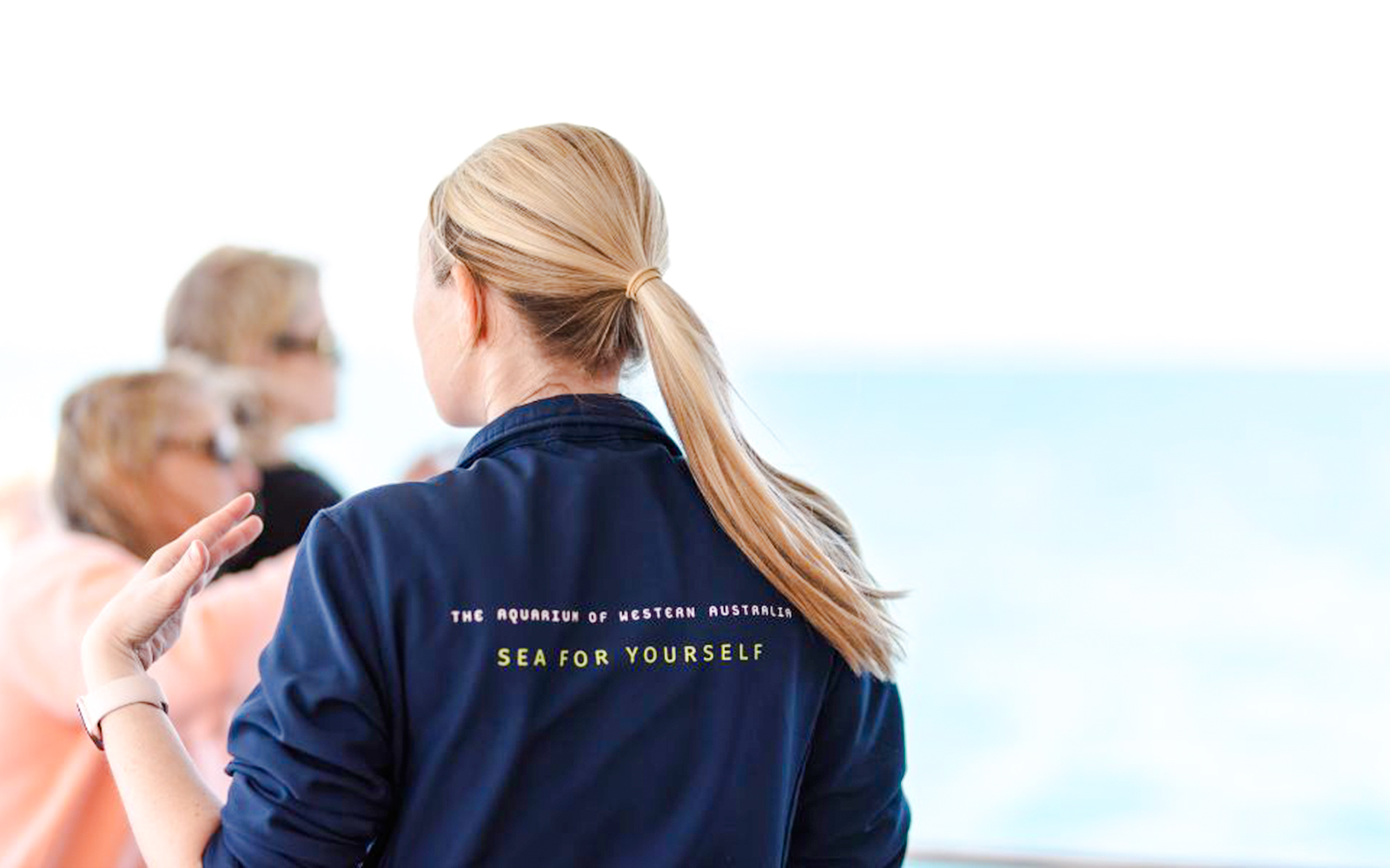 Woman in "Sea For Yourself" jacket gazes at ocean, Aquarium of Western Australia.