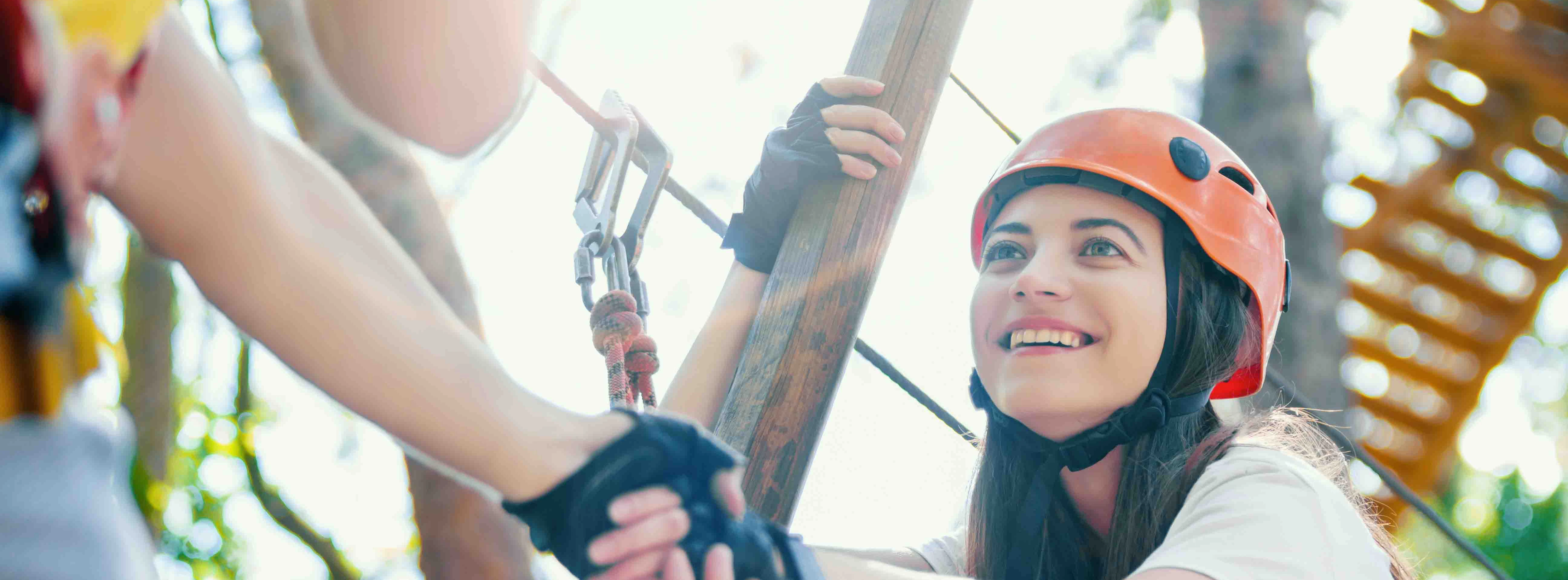 Woman in helmet and harness on a ropes course, holding a guide's hand.