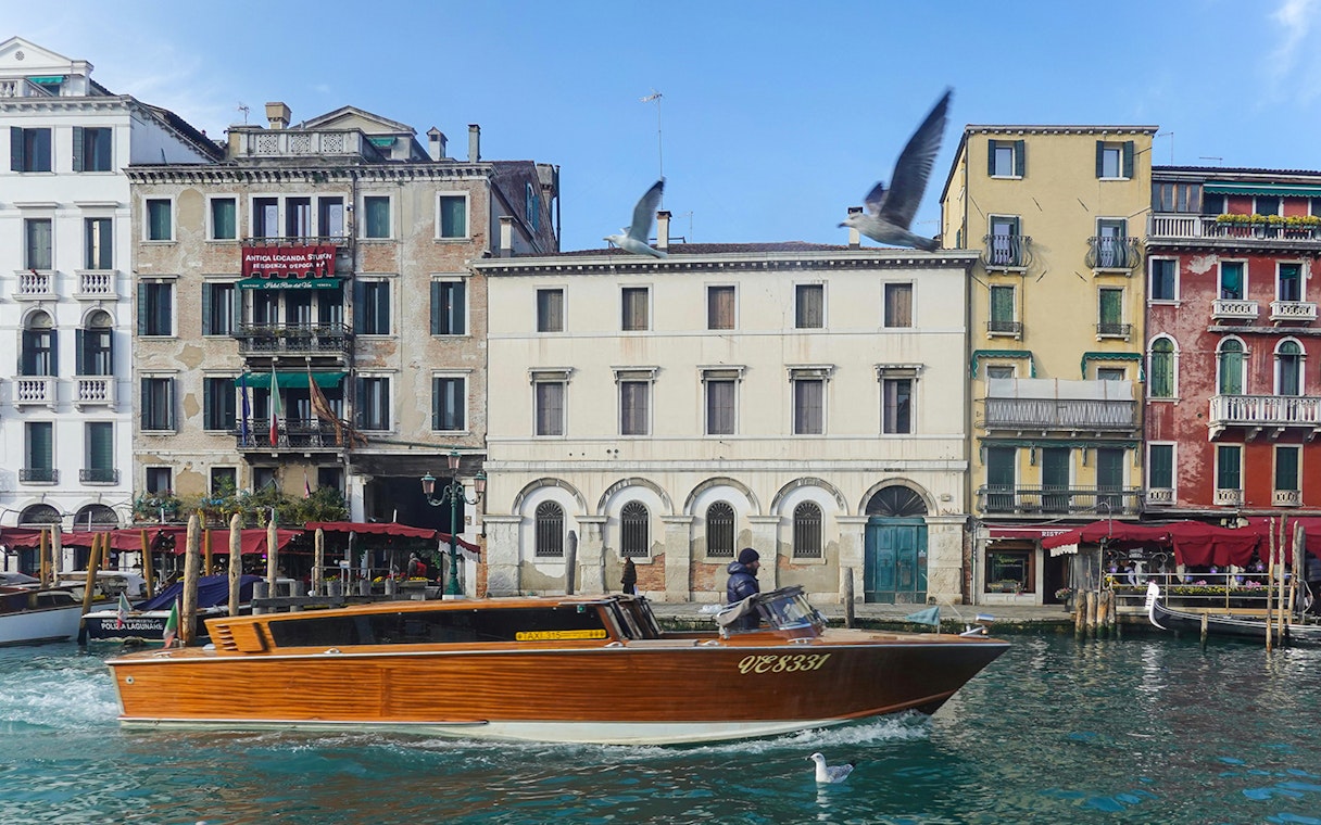 Speedboat cruising Venice canal with historic buildings in the background.