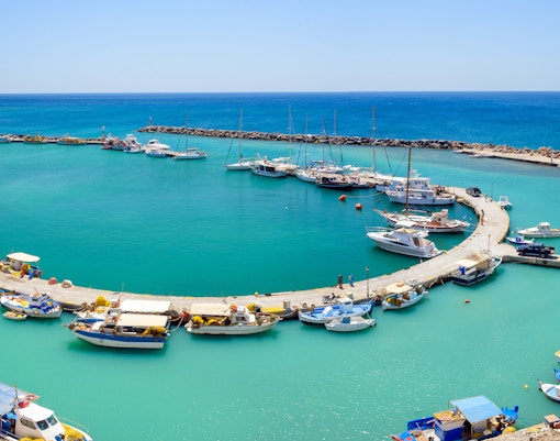 Boats docked at Vlychada port in Santorini, Greece, with clear blue water and a curved pier.