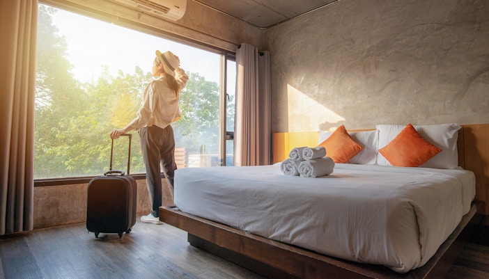 Guest with suitcase in hotel room overlooking forest.