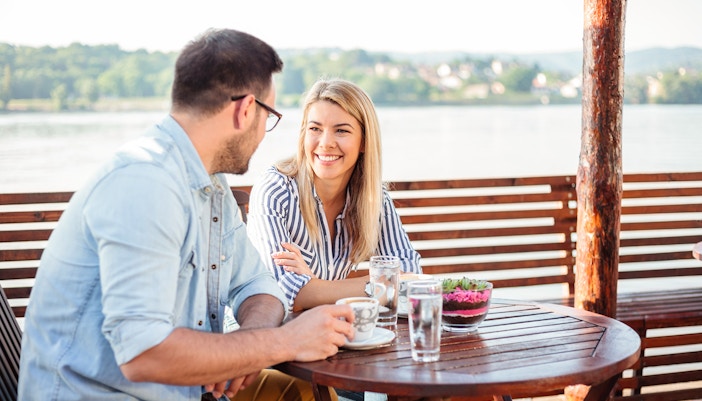 A couple talking and waitng for their meal at a restaurant by the Danube river during the day.