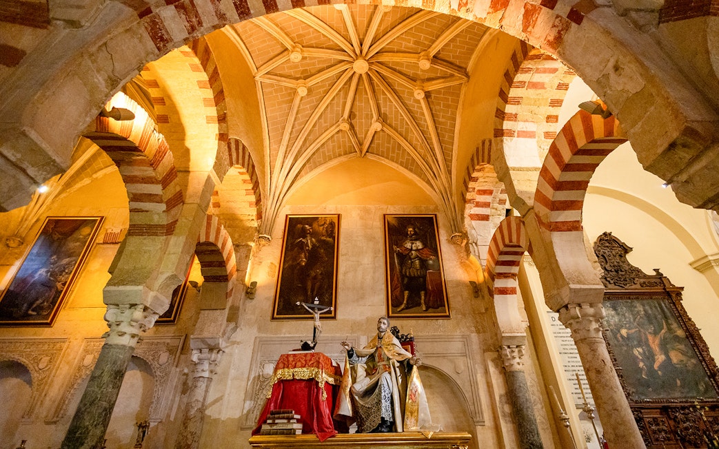 Córdoba Cathedral-Mosque interior with arches and religious statue.