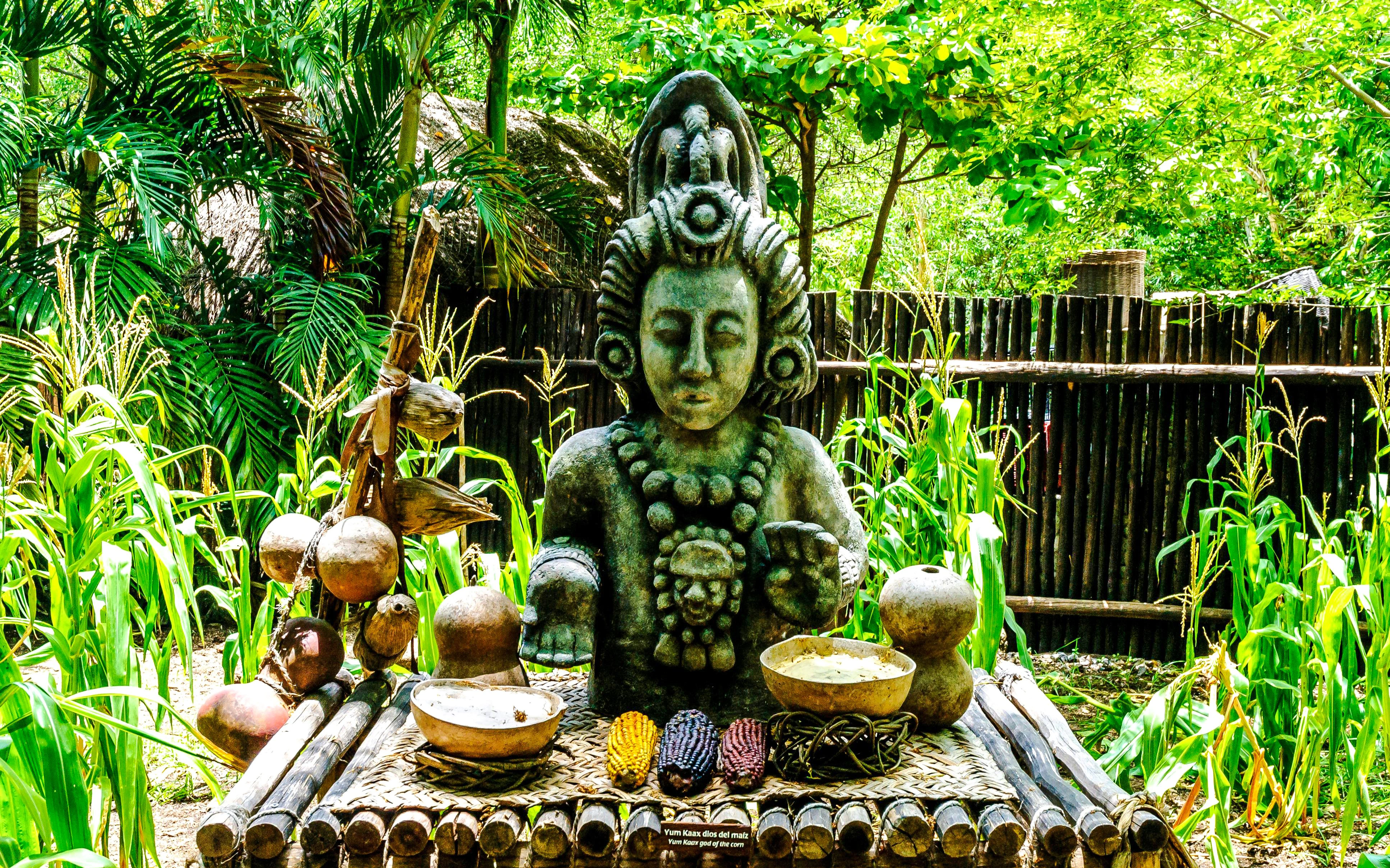Stone statue of Mayan deity surrounded by corn plants at Xcaret.