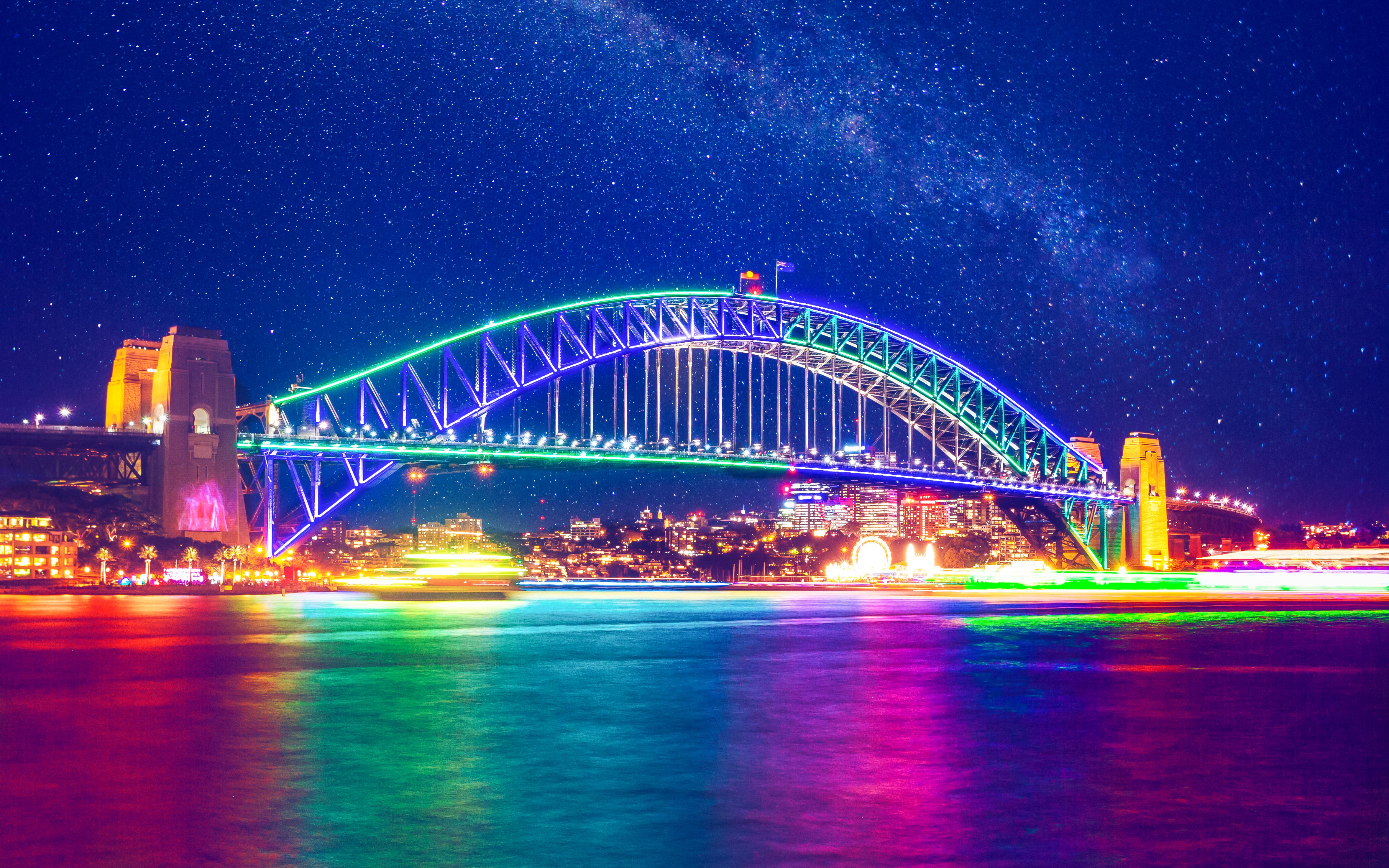 Sydney Harbour Bridge illuminated at night with colorful lights reflecting on the water.