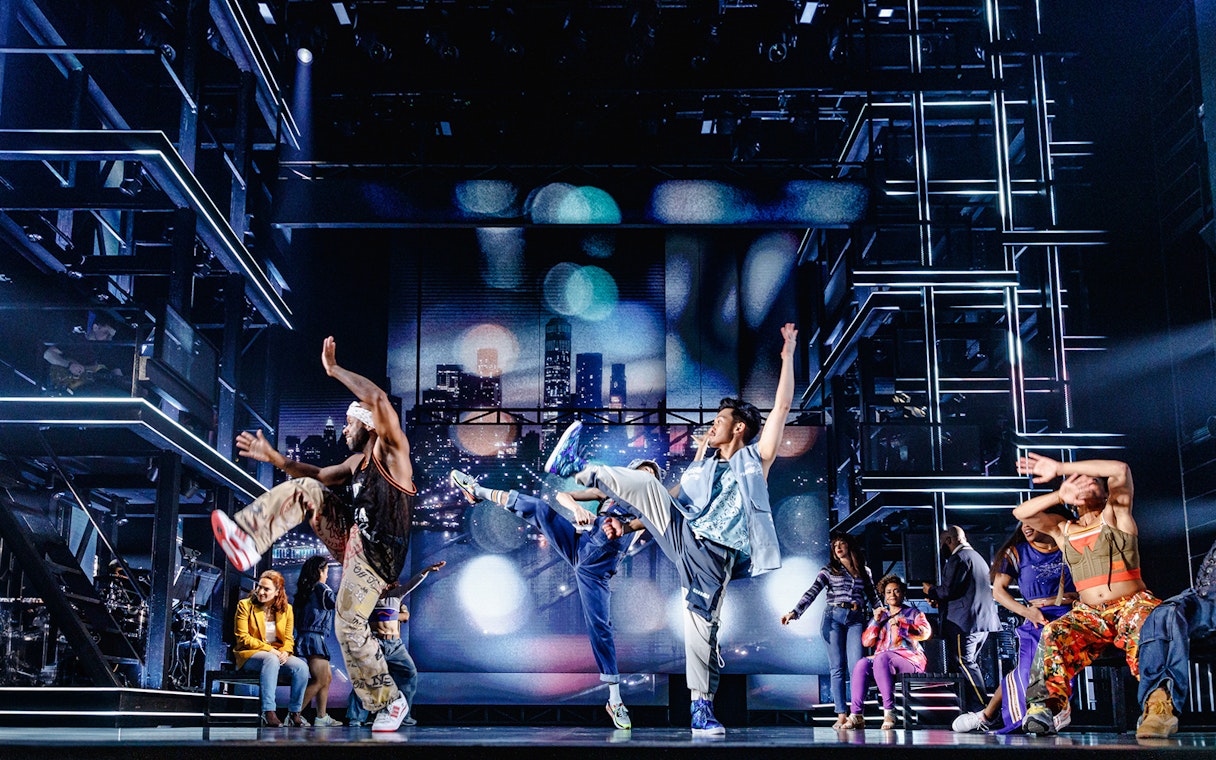 Performers dancing energetically on stage in Hell's Kitchen show.