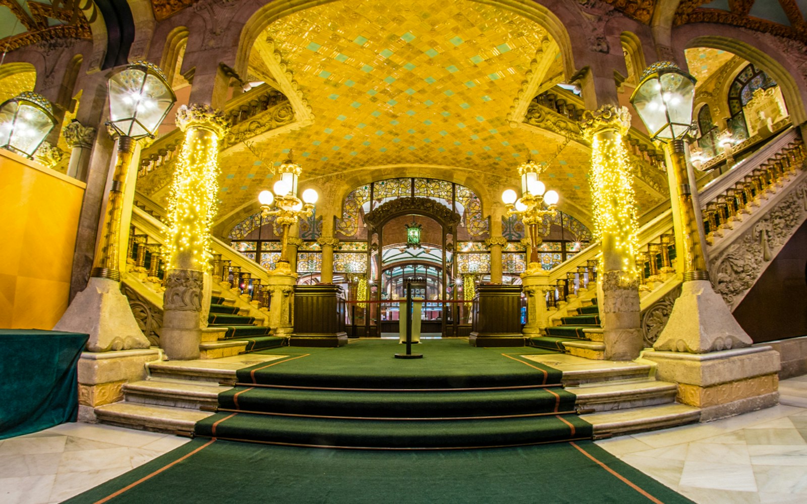 Ornate interior of Palau de la Música Catalana, Barcelona, with grand staircase and decorative lights.