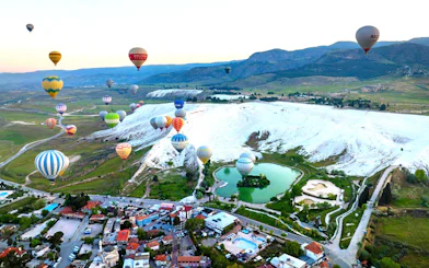 Hot air balloons over Pamukkale's travertine terraces and green landscape.