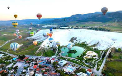 Hot air balloons over Pamukkale's travertine terraces and green landscape.