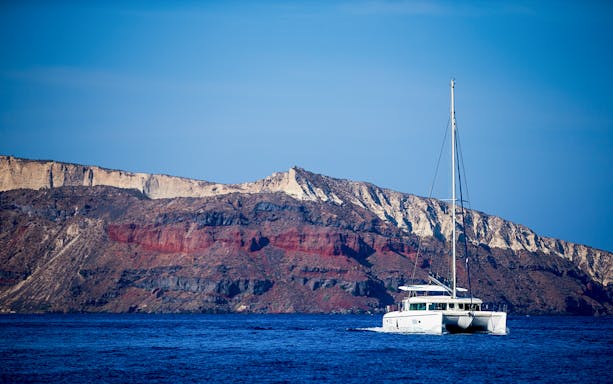 Catamaran sailing near rocky cliffs on a Semi Private Comfort Day Cruise.