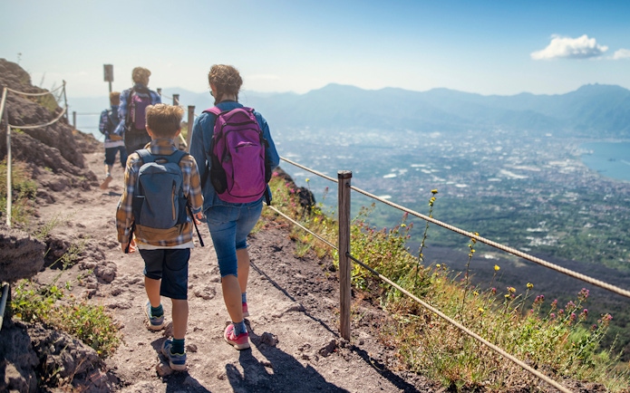 Hikers on Vesuvius volcano trail with view of Naples in the background.