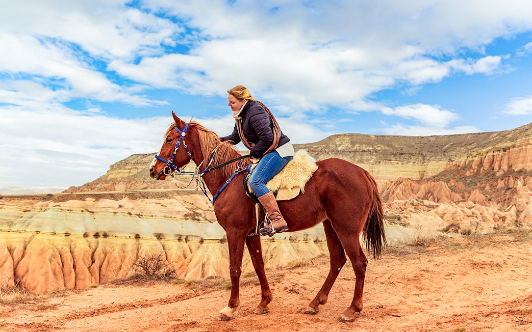 Horseback rider exploring Cappadocia's valleys with unique rock formations.