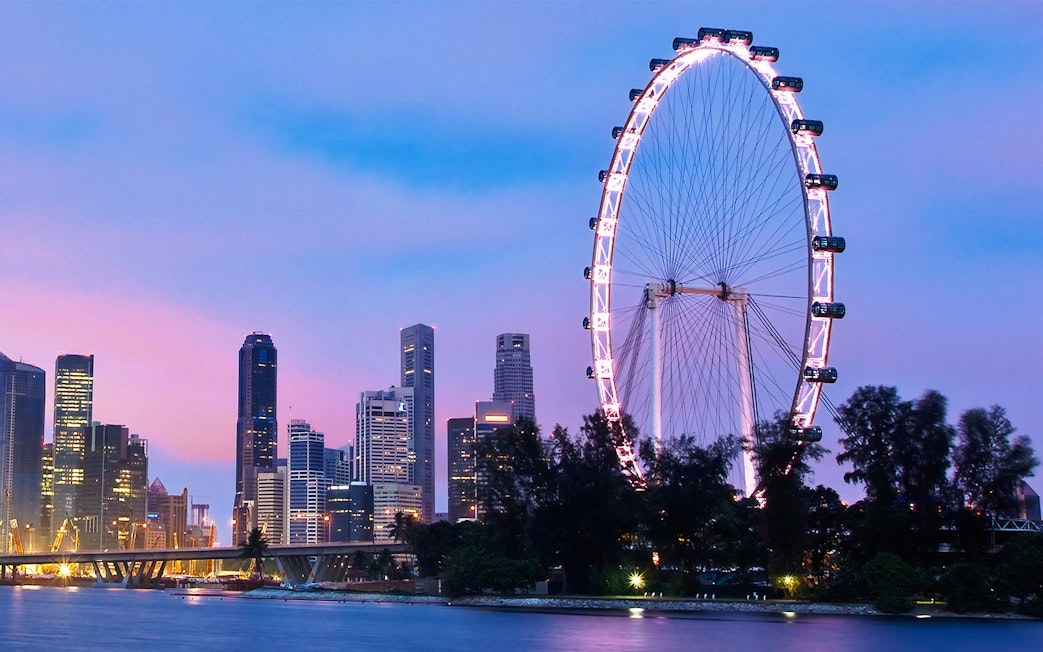 Singapore Flyer illuminated at dusk with city skyline in the background.