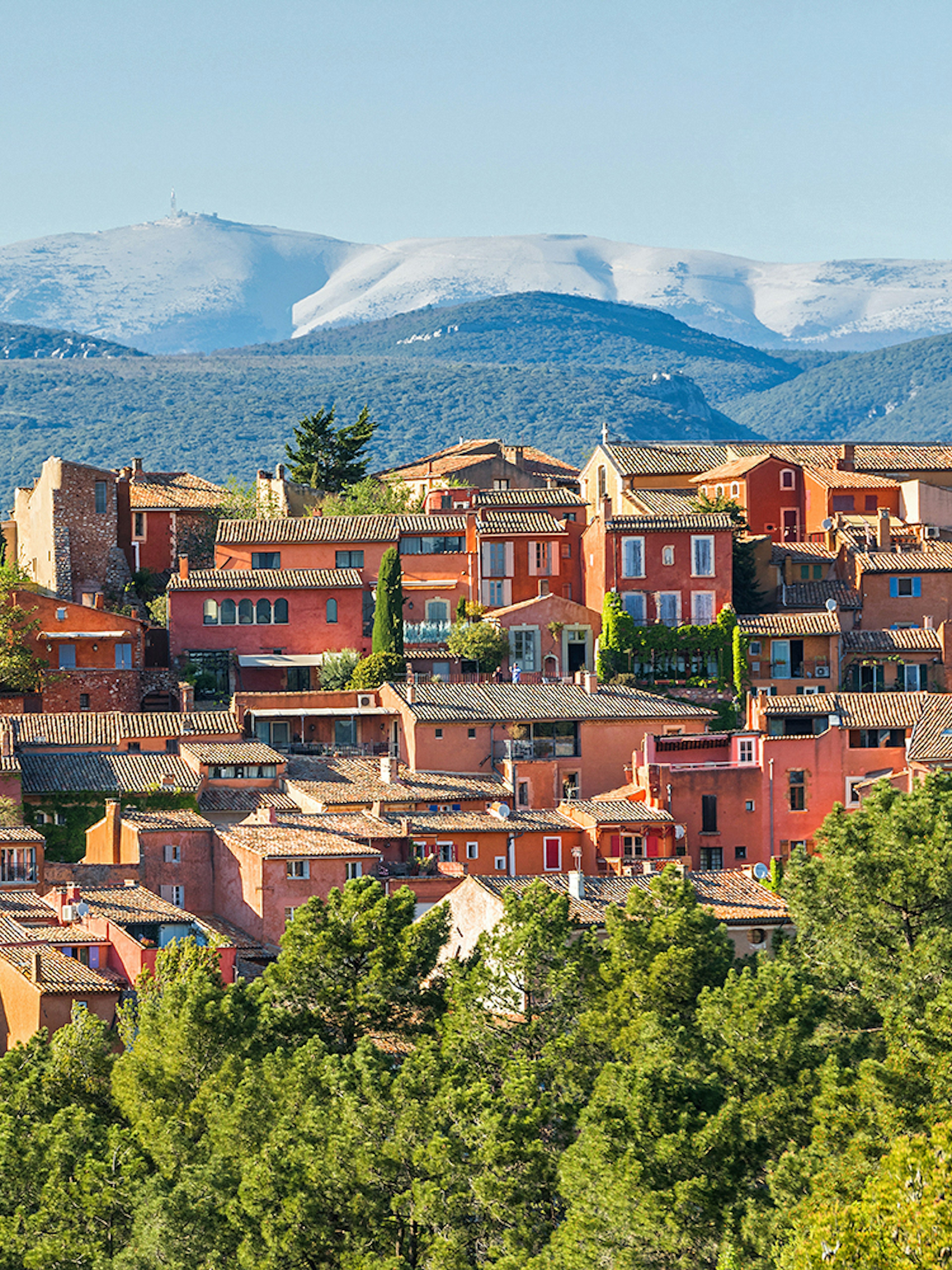 Roussillon village with ochre buildings in Provence, surrounded by green hills and distant mountains.