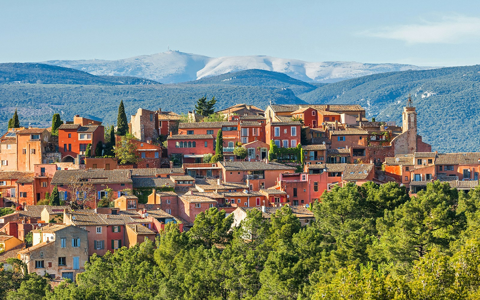 Roussillon village with ochre buildings in Provence, surrounded by green hills and distant mountains.