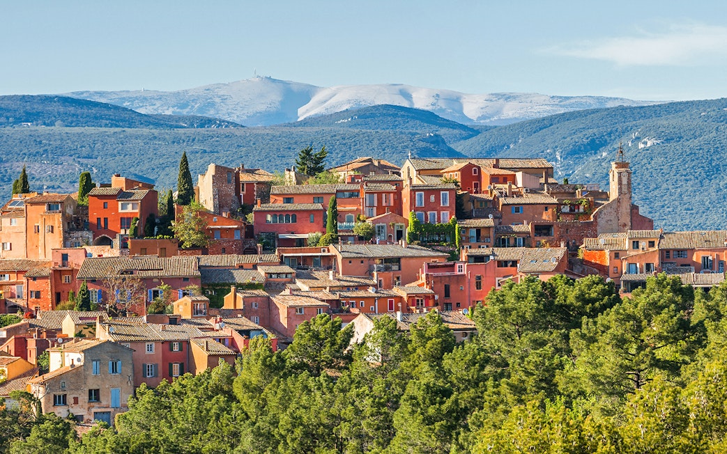 Roussillon village with ochre buildings in Provence, surrounded by green hills and distant mountains.