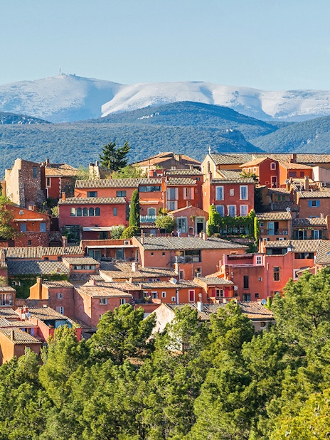 Roussillon village with ochre buildings in Provence, surrounded by green hills and distant mountains.