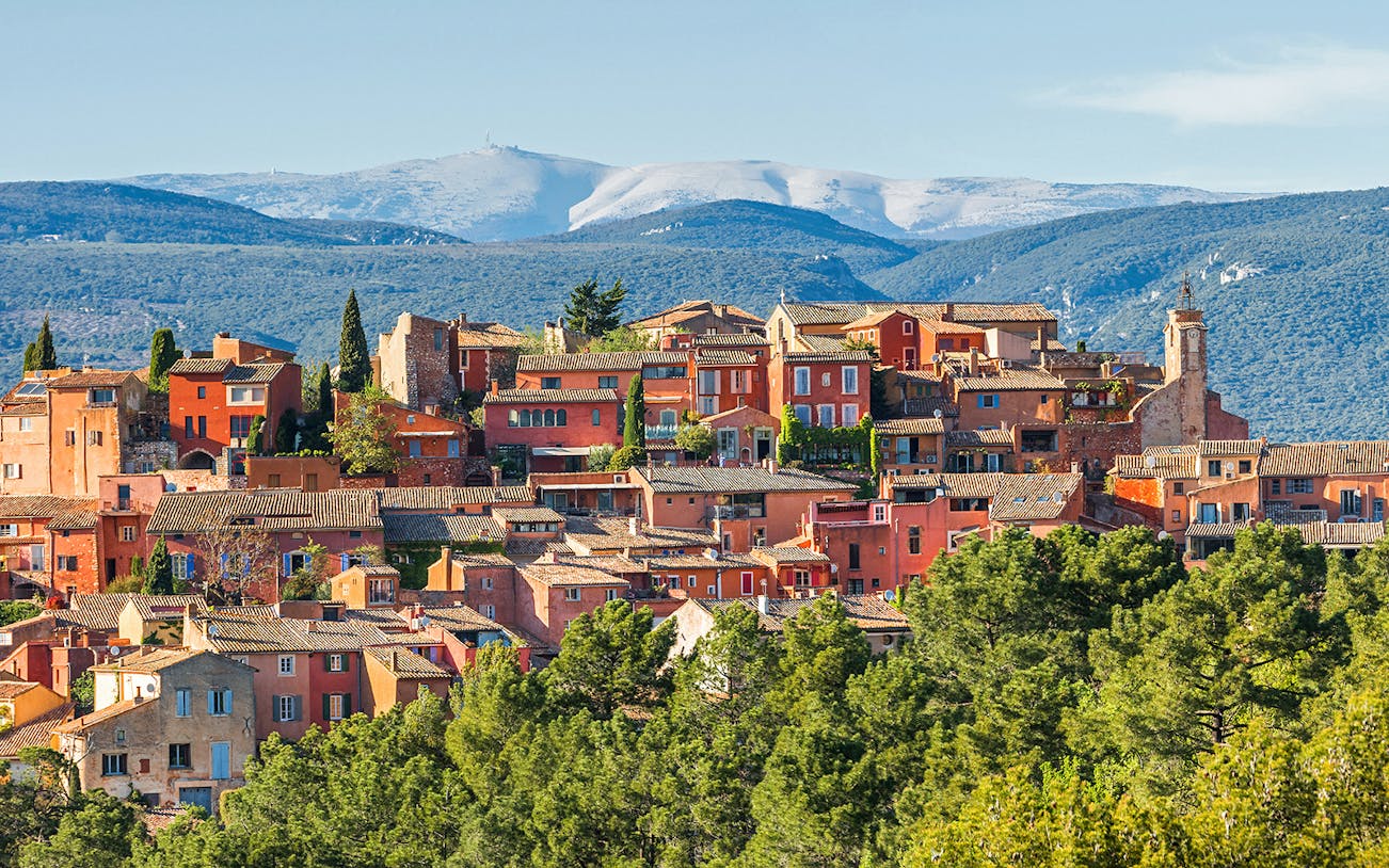 Roussillon village with ochre buildings in Provence, surrounded by green hills and distant mountains.