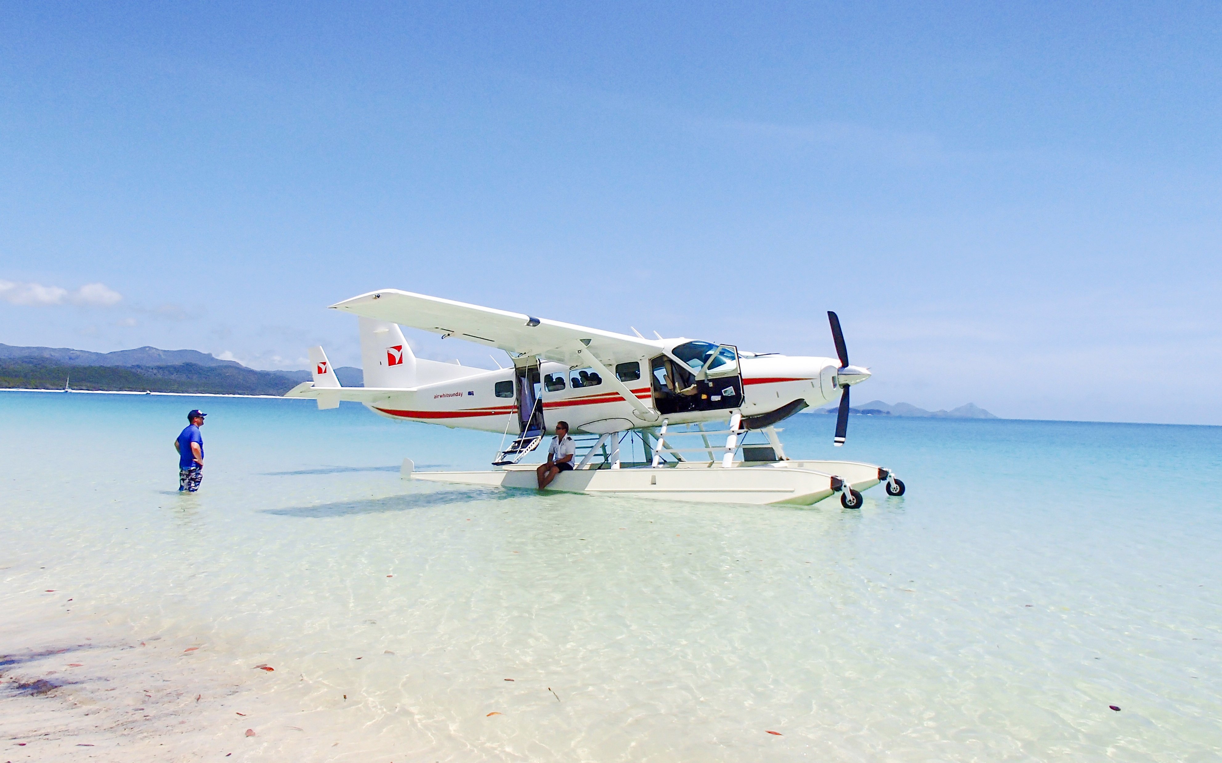 Seaplane on clear waters at Airlie Beach with a person standing nearby.