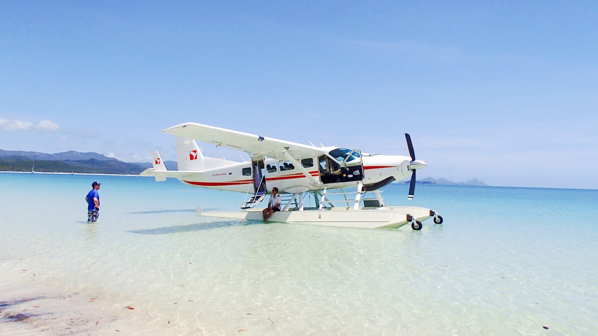Seaplane on clear waters at Airlie Beach with a person standing nearby.