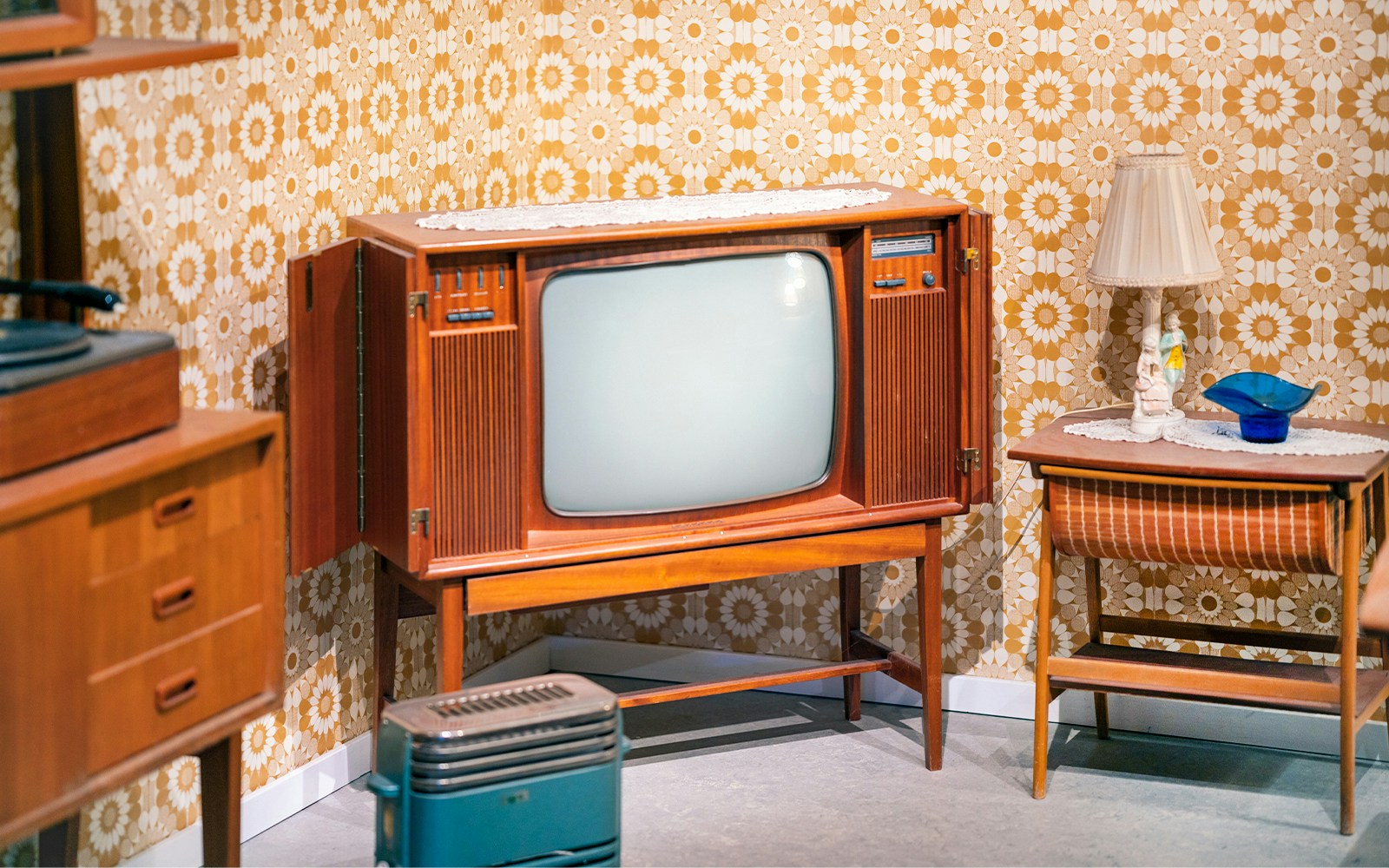 Old television in a retro furnished room with floral wallpaper.