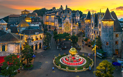 Central square of medieval city in Ba Na Hills Park, Da Nang, with illuminated buildings at sunset.