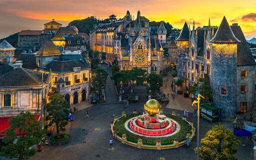 Central square of medieval city in Ba Na Hills Park, Da Nang, with illuminated buildings at sunset.