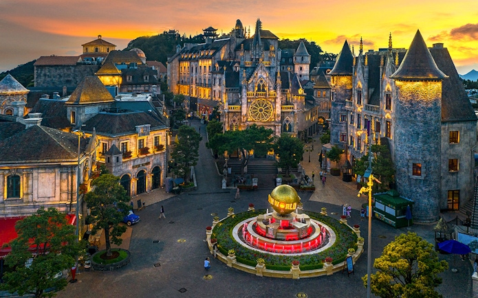 Central square of medieval city in Ba Na Hills Park, Da Nang, with illuminated buildings at sunset.