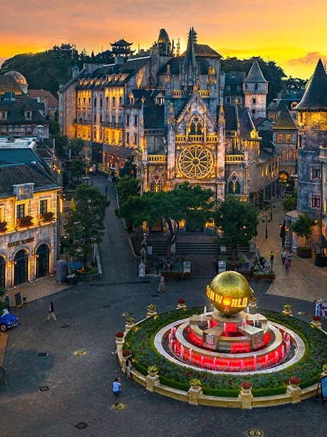 Central square of medieval city in Ba Na Hills Park, Da Nang, with illuminated buildings at sunset.