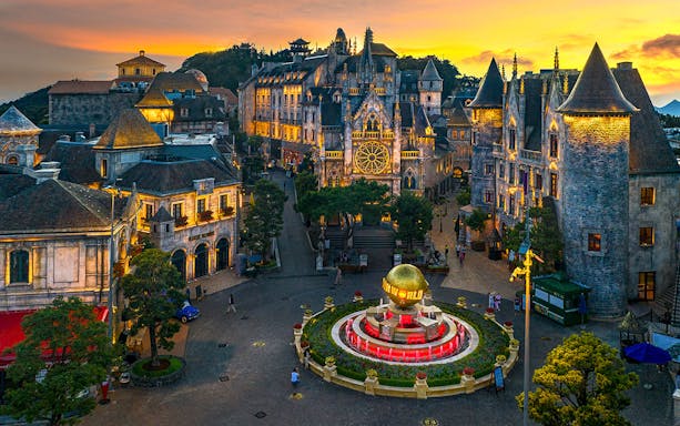 Central square of medieval city in Ba Na Hills Park, Da Nang, with illuminated buildings at sunset.