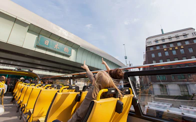 Tokyo hop-on hop-off bus passing under Nihonbashi bridge with passengers pointing.